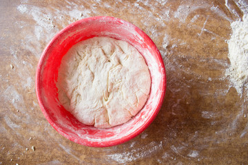 Dough and flour on wooden table in red plate