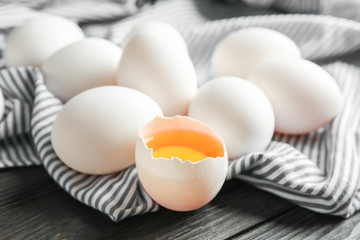 Chicken eggs in kitchen towel on wooden background, space for text