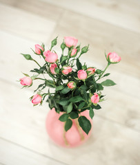Sweet pink roses flowers in vases on beige painted wooden background.