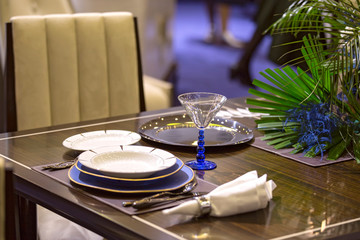 Table setting in blue color in the restaurant, plates, beautiful glasses, flowers