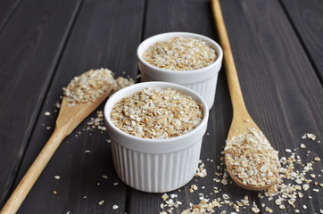 Rolled oats in bowls and spoons on dark wooden table background