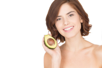 Food for healthy looks. Horizontal portrait of a beautiful young woman smiling and holding half an avocado over the side of her face isolated on white