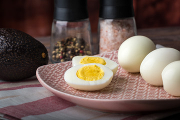 Hard boiled eggs on a plate with avocado, salt and pepper in background