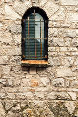 Fototapeta na wymiar Window with arch and grille on stone wall