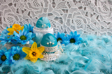 Wielkanocne biało-błękitne tło z koronką, błękitnymi pisankimi , piórami i kwiatami
