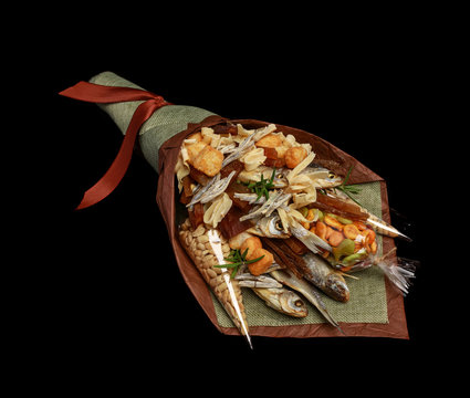Original bouquet consisting of dried salted fish, salted peanuts, crackers, dried bread and other beer snacks isolated on black background as male gift. Left view