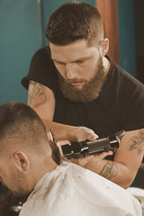 Fototapeta premium Careful work. Vertical portrait of a barber working on the haircut with a trimmer