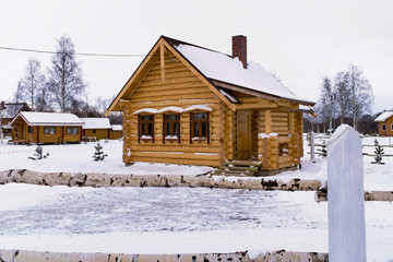 One-storey wooden house with brick chimney in winter with a fence from birch trunks in Russia