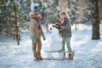 Children build a snowman. Boys building a snow man playing outside on a sunny snowy winter day. Outdoor family holiday on the Christmas holidays. Boy and girl playing snowballs.