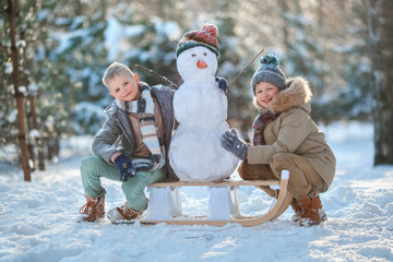 Children make a snowman. Children building a snow man playing outside on a sunny snowy winter day. Outdoor family holiday on the Christmas holidays. Boys play snowballs. Winter clothes