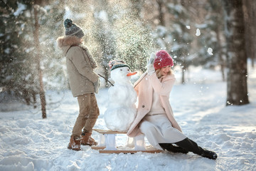 A happy family! Mom and child on a winter walk in nature sculpt a snowman playing snowballs in a...