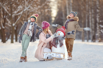 Mom and children in the winter forest play snowballs and make a snowman. Walking in the winter holidays.