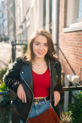 Portrait of a beautiful girl on a sunny day. Streets of Amsterdam. Great mood. A girl enjoys her lifestyle. She is wearing a red T-shirt, jeans and a leather jacket.