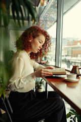 Smiling red hair woman reading book at coffee shop