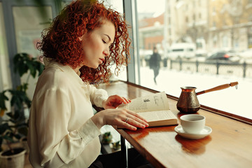 Smiling red hair woman reading book at coffee shop