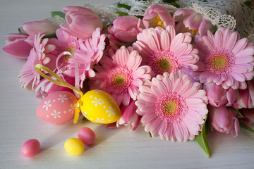 Greeting card background with a bouquet of pink gerbera flowers and tulips, Easter egg decors