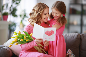happy mother's day! child daughter   gives mother a bouquet of flowers to tulips and postcard.