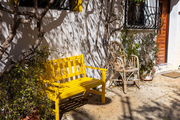 A small courtyard with a yellow wooden bench and a wicker chair and pots with plants in the old city of Finestrat Spain