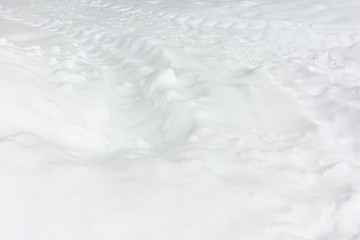 Fresh white snow with traces from the tractor. Abstract background with a snowy texture.