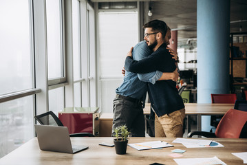 Two business colleagues hug and congratulate each other with success in their office