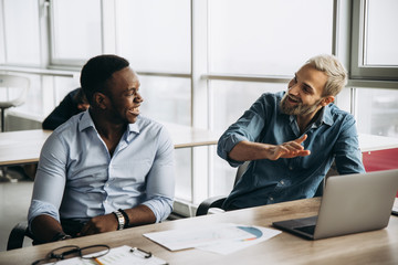 Successful managers in stylish formal clothes are sitting at the table and discussing new company...