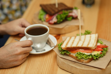 man takes a cup of coffee from a wooden table, on which lies a sandwich