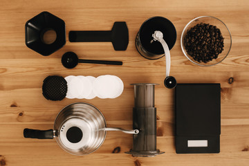 Steel kettle, scale, filter, manual grinder, aeropress, coffee beans top view. Alternative coffee brewing method, flat lay. Stylish accessories and items for alternative coffee on wooden table.