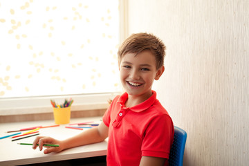 cute happy brunette 9-10 years old in red shirt drawing at home at table with colored pencils