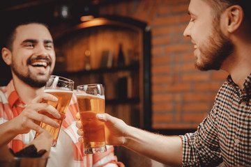 Friends, young guys met at pub, they drink alcohol, clanging bottles of beer. Concept male friendship, weekend