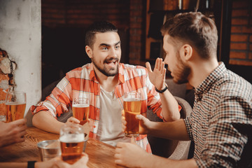 Live conversation. Very emotional young bearded man with piercing tells story to his friend in pub over mug of beer.