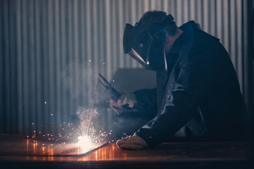 Professional welder performs welding work on metal in protective mask. Industrial worker concept