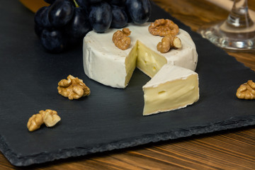 Camembert cheese in a dark tray next to sweet blue grapes nuts and honey