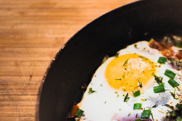 Scrambled eggs with tomatoes and green onion in a pan on a wood Board