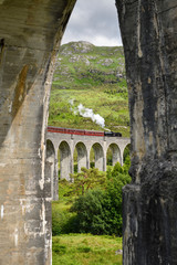 View of heritage Jacobite Steam Train through concrete columns of the Glenfinnan viaduct in the Scottish Highlands Scotland UK