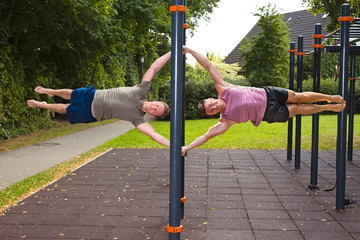 Two young men doing calisthenics exercises on bar outdoors.
