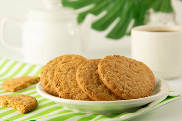 Oat Cookies and coffee breakfast, or coffee break. Oatmeal healthy biscuits. Green monstera, plam leaves. Copy space. Bright background. Food.