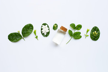 Bottle of essential oil with jasmine flower and leaves on white.