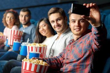 This one is for a good memory. Group of happy cheerful friends taking selfie together sitting in a local movie theater