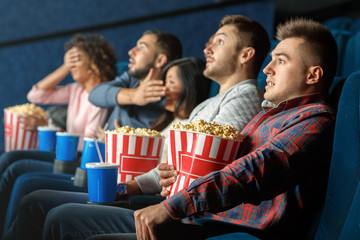 Obraz premium Horror movies marathon. Young man looking scared sitting at the movie theater with his friends