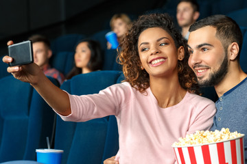 Take a selfie with me. Horizontal shot of a cute young couple taking selfie together using smartphone while spending time in a local movie theater