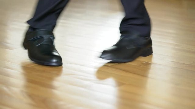 Legs of a man in black shoes dancing elements of dubstep on the brown floor background. View shot looking straight at the shoes and legs in black trousers.