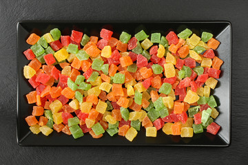 Small colorful candied fruit pieces of papaya, mango, kiwi, pineapple, lying on a black ceramic plate on a black stone surface. Macro