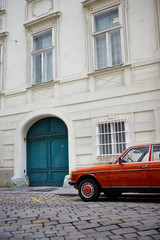 Fototapeta na wymiar Retro orange car on pavement near the old white building. Cyan door