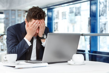 Nothing goes right today. Portrait of an upset man wearing suit sitting with his face in his hands in front of his laptop