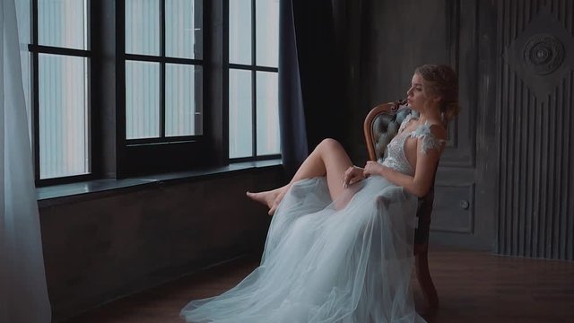 majestic and proud princess girl in white silver dress with long train tired sitting on chair, lady shows off her lifted bare legs on bylets, gentle stylish image of graduate 2019