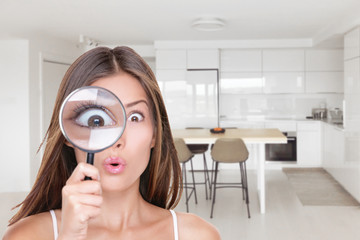 Home shopping funny inspection woman searching through magnifying glass at kitchen furniture. Deal hunting bargain hunter Asian girl looking at real estate new homeowner inspecting interior design. - obrazy, fototapety, plakaty