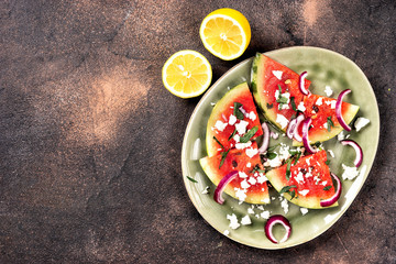 Fresh summer grilled watermelon peaces with feta cheese, mint, onions on brown background