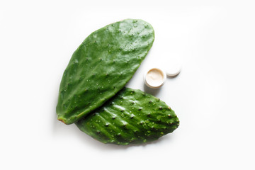 Closeup container of cream on a green leaf of a prickly pear cactus on a white background. On the cactus large drops of water.