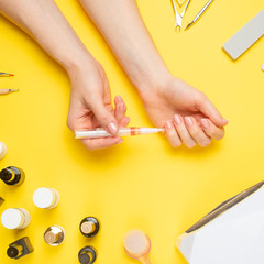 Nail art in the luxurious beauty salon. Gel for modeling nails. A woman receives a manicure by a beautician. On a yellow background, care and care of nails.