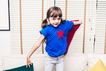 Little girl in superhero costume having fun and playing superheroes at home
